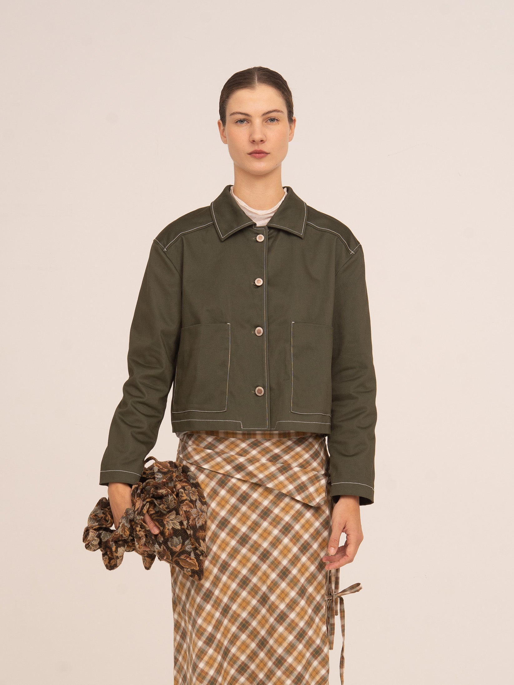 Chaqueta corta en color verde oliva con cierre de botones frontales, cuello clásico y pespuntes visibles, de silueta recta y mangas largas.