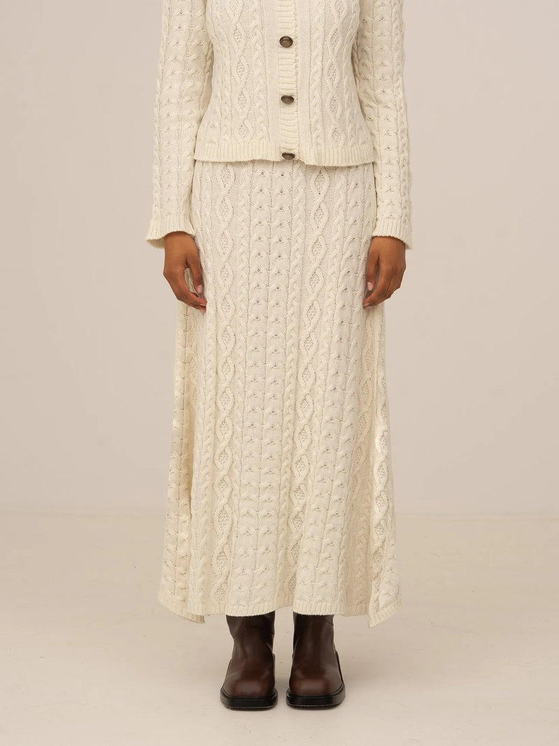 Falda larga blanca de punto con textura trenzada y corte recto, presentada sobre modelo en estudio con fondo neutro.