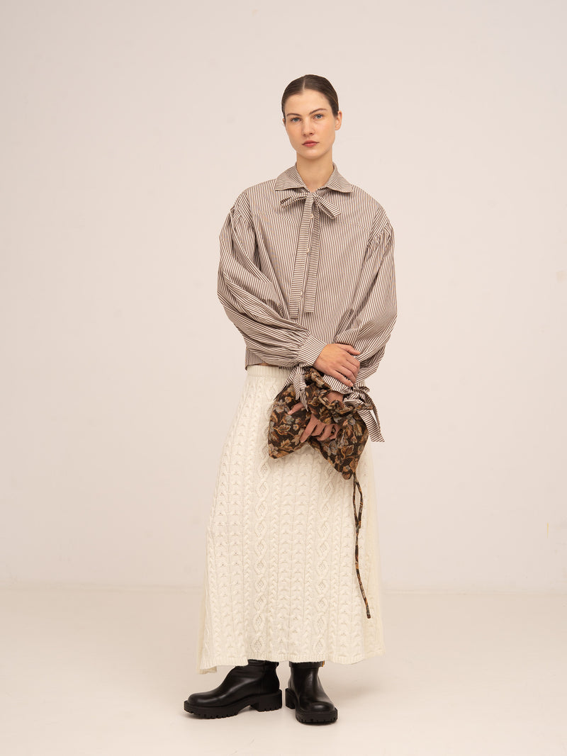 Bolso tipo pouch en tonos marrones con estampado floral, llevado en la mano, de estilo elegante y femenino.