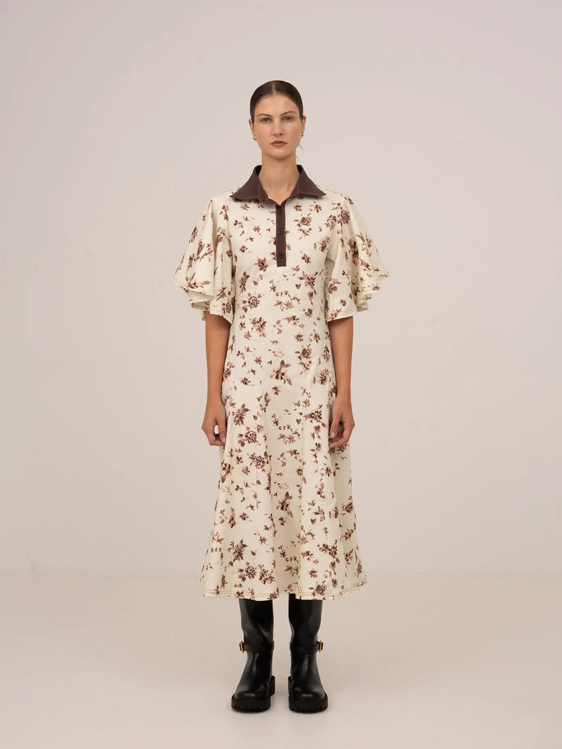 Vestido midi con estampado floral en tonos marrón sobre fondo claro, con cuello camisero en contraste, manga corta amplia y silueta recta de caída fluida.