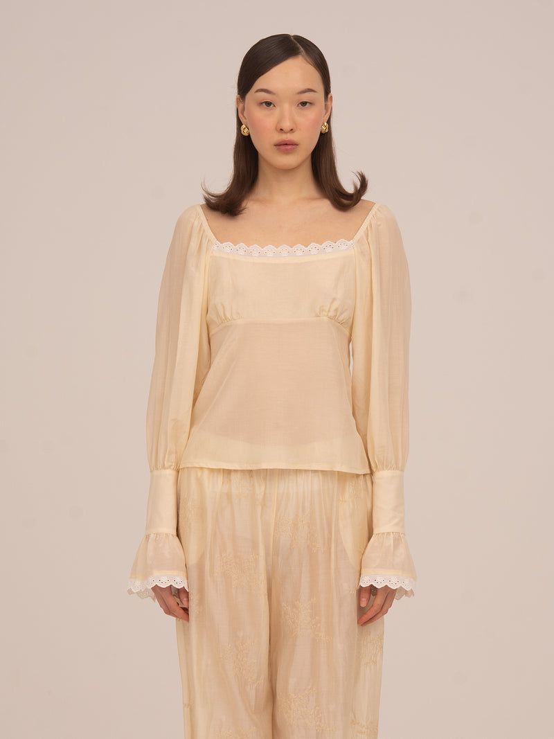 Blusa color crema de Carmen Says con escote recto y detalle de encaje, manga larga semitransparente y diseño romántico ideal para looks elegantes y ocasiones especiales.