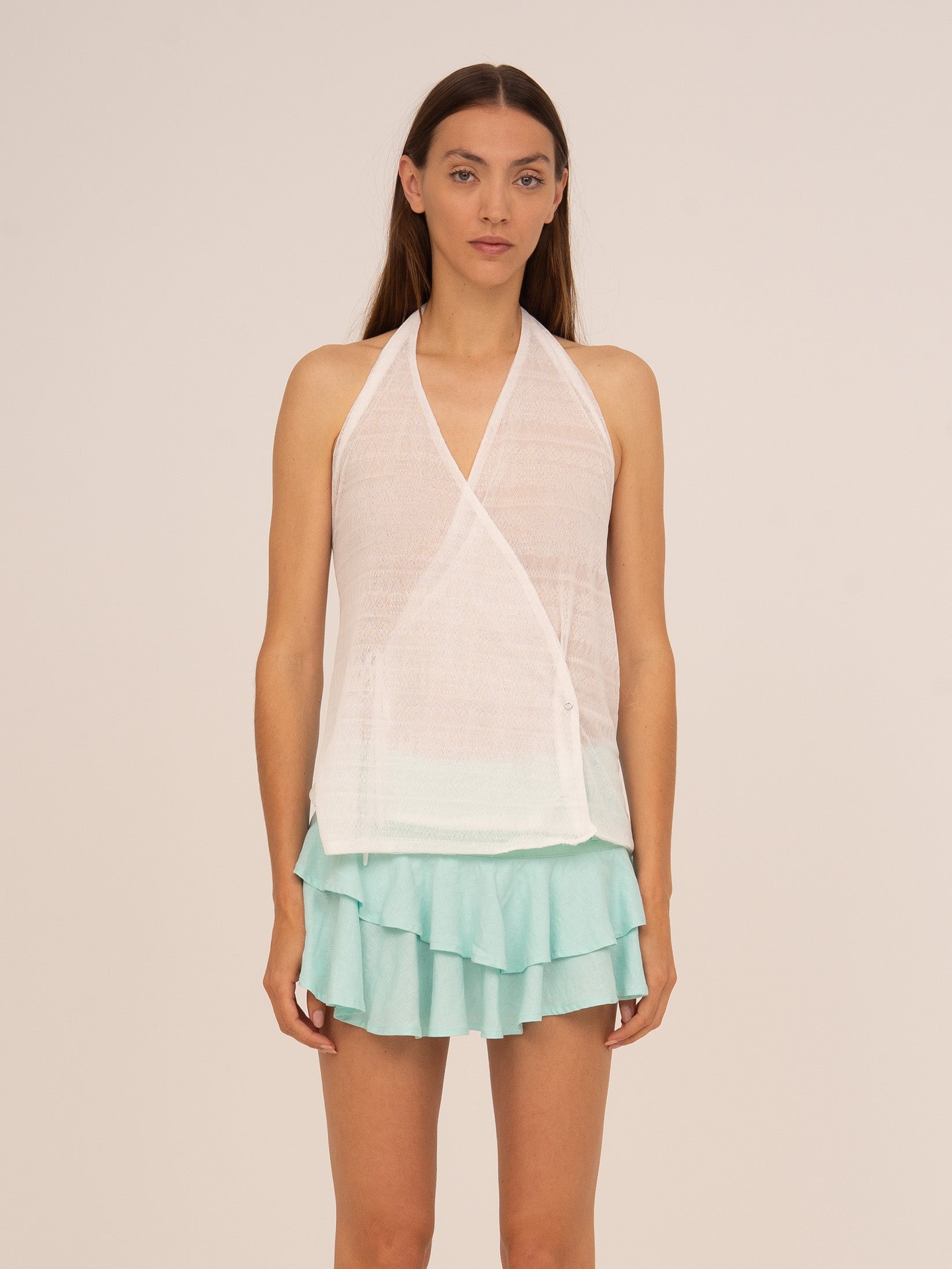 Top blanco de estilo halter con diseño cruzado y escote drapeado, confeccionado en tejido fluido y ligero. Una prenda femenina y sofisticada ideal para looks elegantes de verano.