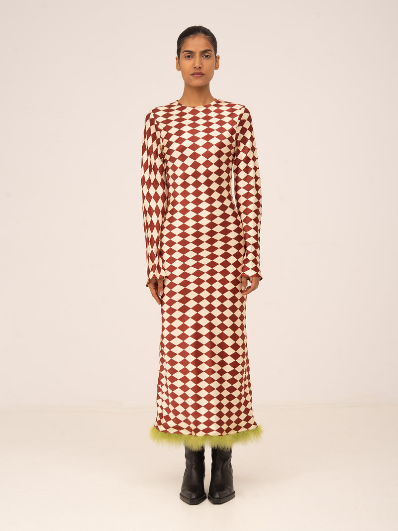 Vestido largo con estampado geométrico de rombos en tonos rojo y crema, mangas largas y detalle de plumas verdes en el bajo.