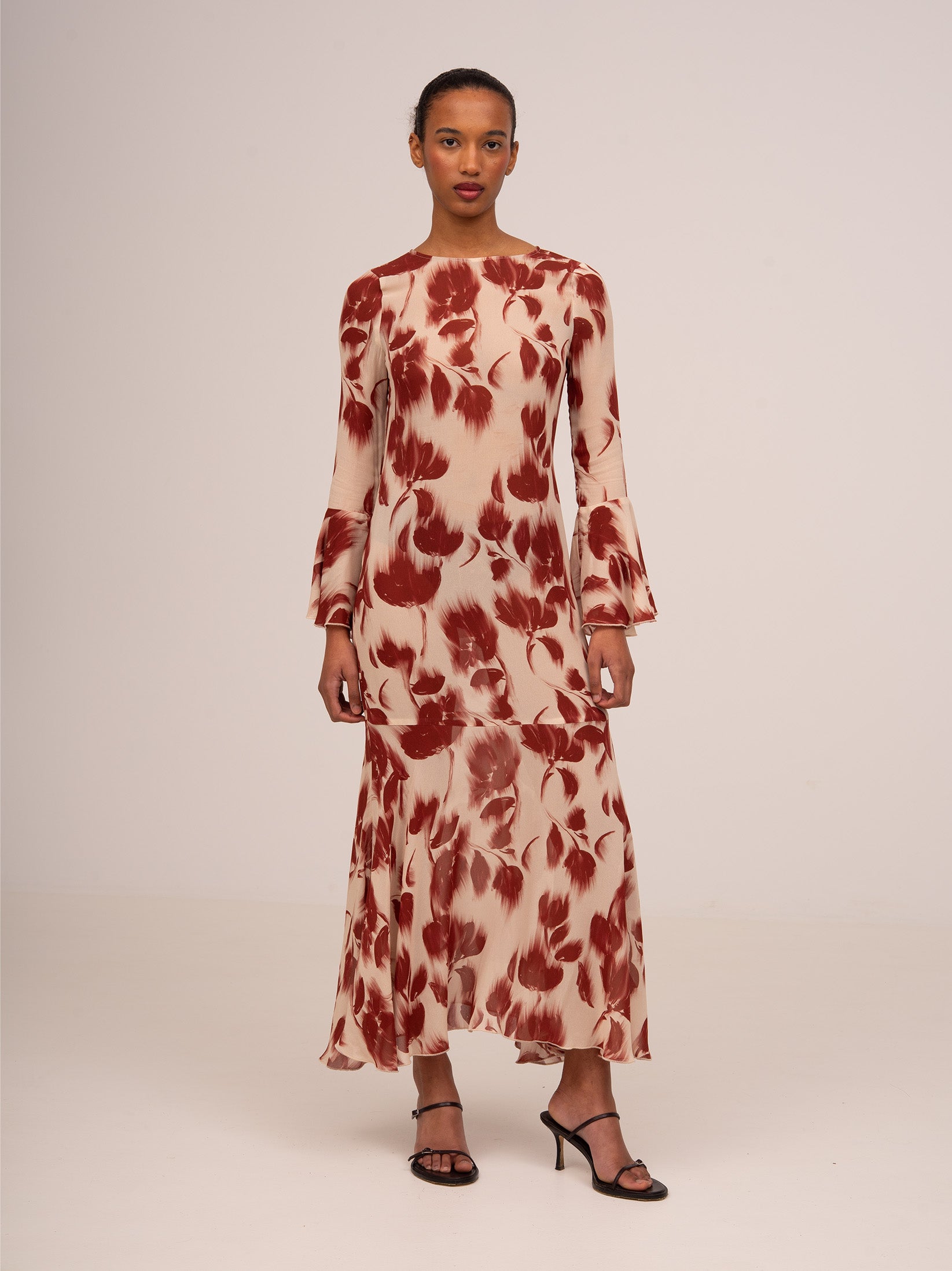 Vestido midi floral rojo sobre fondo crema, silueta entallada, mangas largas con volantes acampanados y cierre de botón en la espalda.