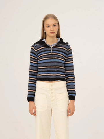 Top de punto a rayas en tonos azul y negro, con cuello tipo polo, manga larga y silueta ajustada, presentado sobre modelo en estudio con fondo neutro.