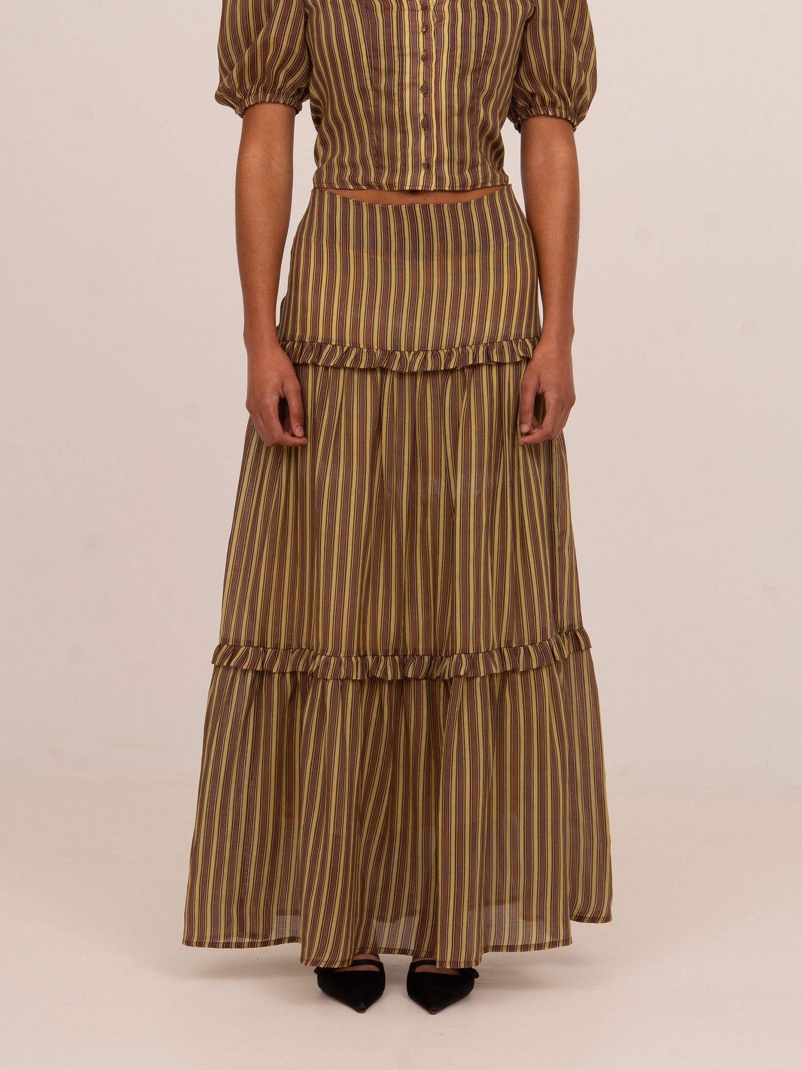 Falda larga de mujer en tonos marrón y verde con estampado de rayas verticales, diseño fluido con volantes y acabado ligero.