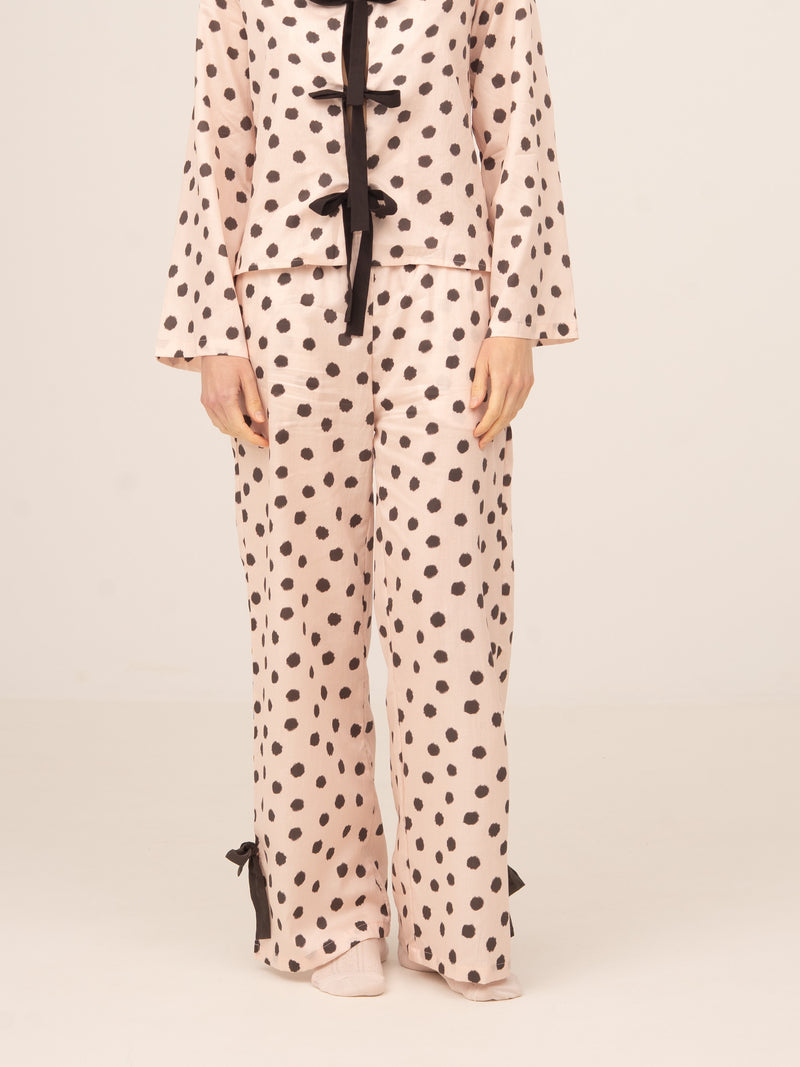 Modelo femenina vistiendo pantalón de pijama en color claro con estampado de lunares negros y detalles de lazos en el bajo, conjunto de inspiración loungewear, fotografiada de frente sobre fondo neutro.