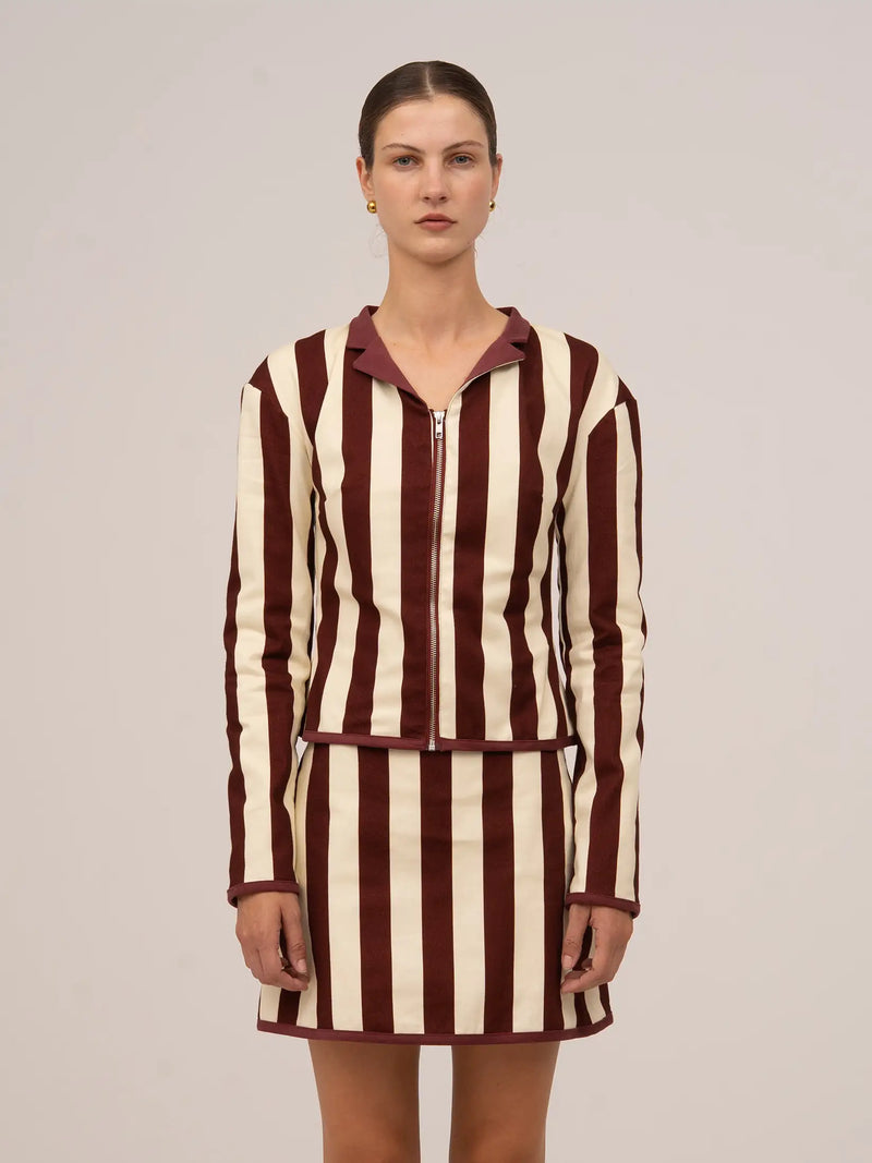 Chaqueta de manga larga con rayas verticales en tonos burdeos y crudo, cierre frontal con cremallera y cuello camisero.