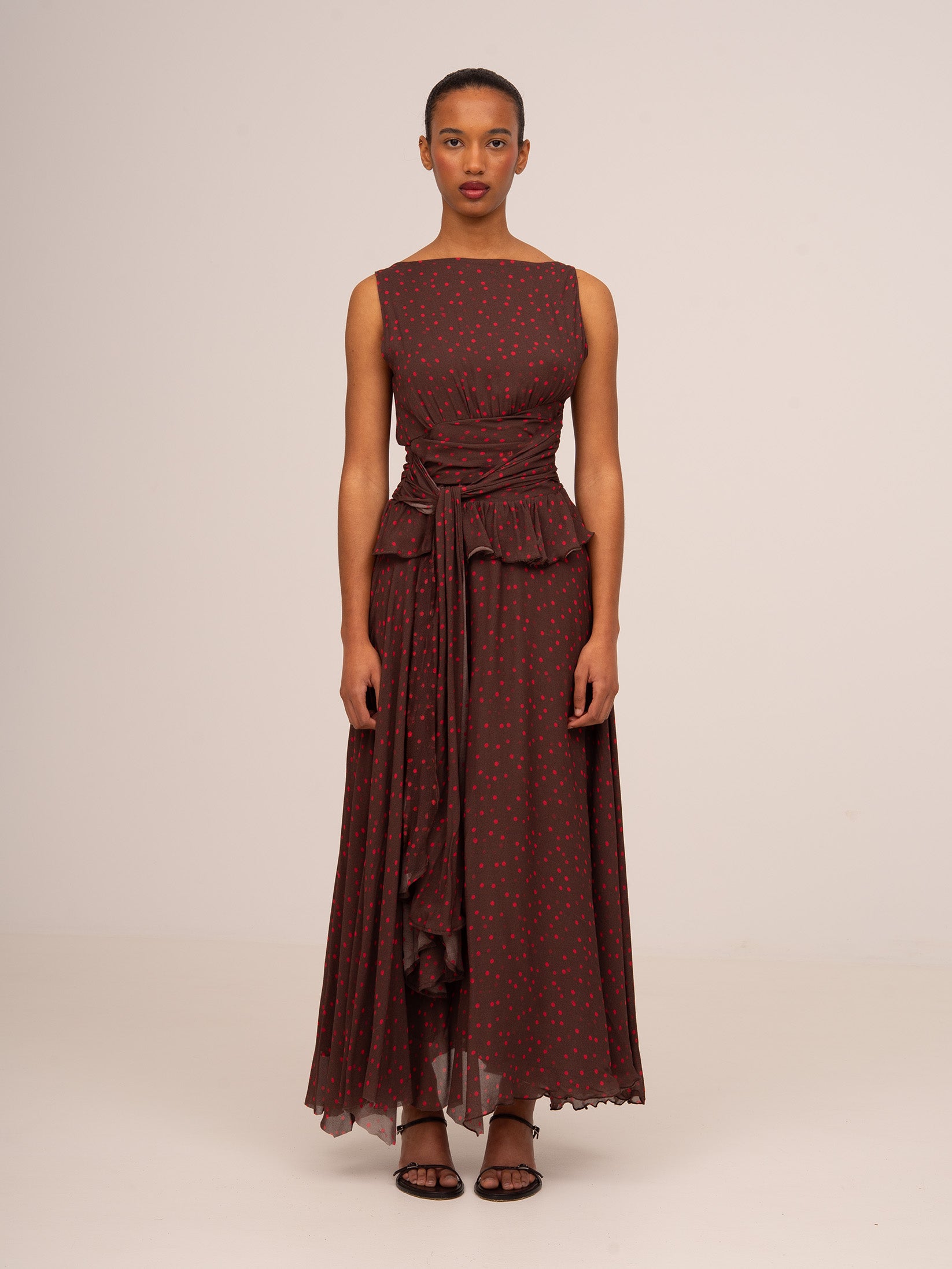 Vestido largo de mujer en color marrón con estampado de lunares rojos, diseño sin mangas y detalle drapeado en la cintura.
