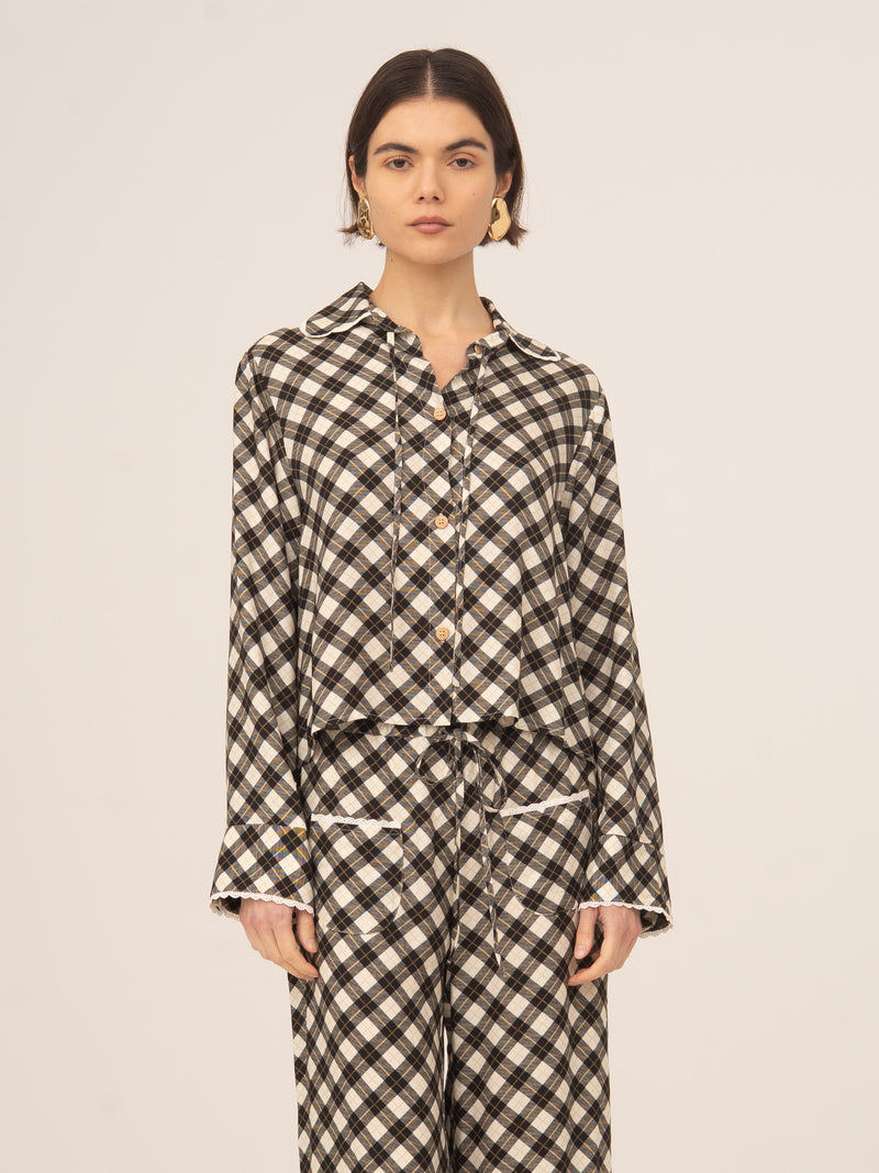 Modelo femenina posando de frente con camisa de manga larga y corte recto, estampado geométrico tipo argyle en tonos neutros, cuello camisero y cierre de botones, combinada con pantalón a juego sobre fondo claro y neutro.