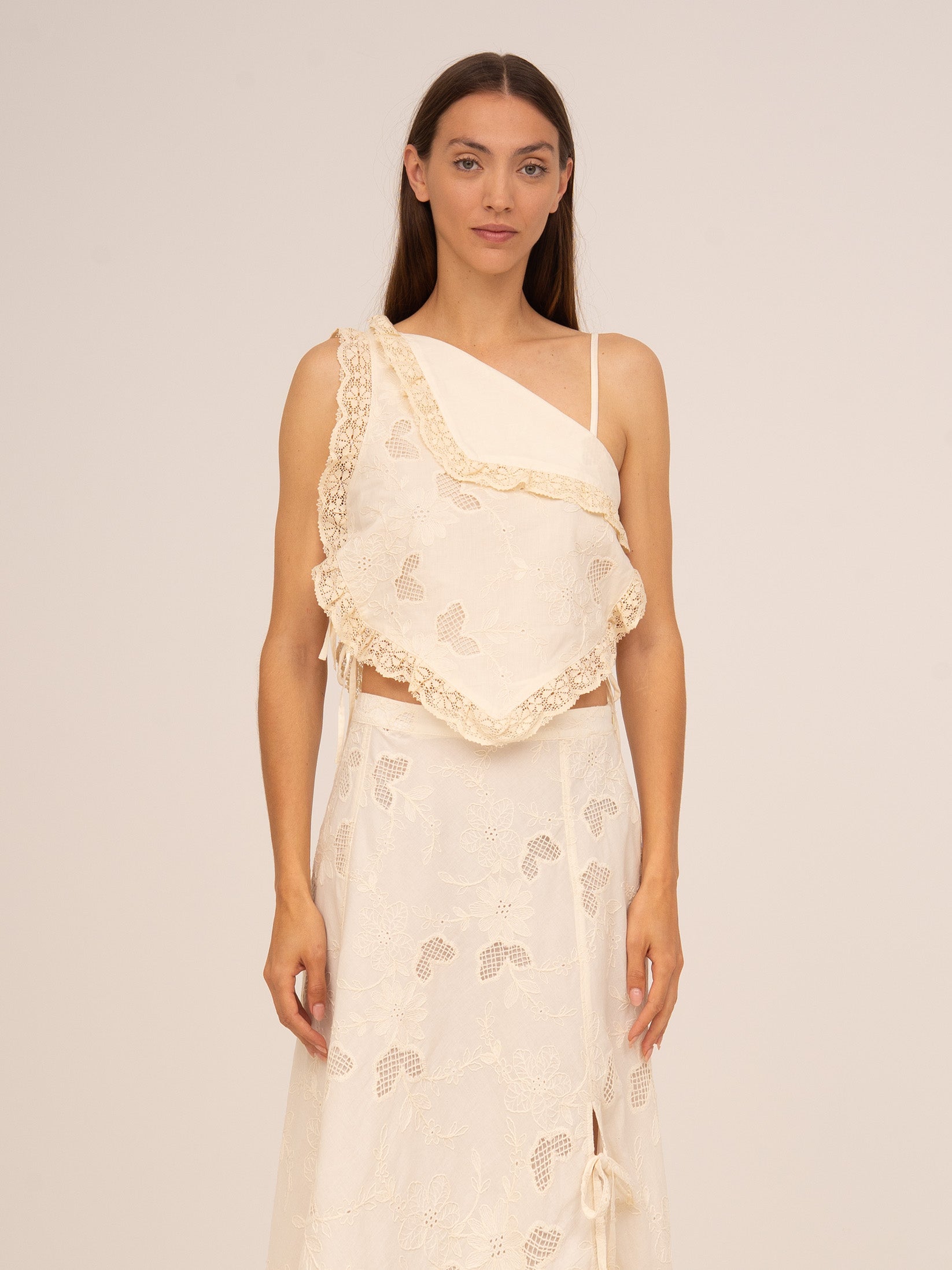 Top asimétrico en color crema con detalle de bordados delicados y silueta ajustada. Un diseño sofisticado y femenino que aporta un toque artesanal y contemporáneo a cualquier look de verano.