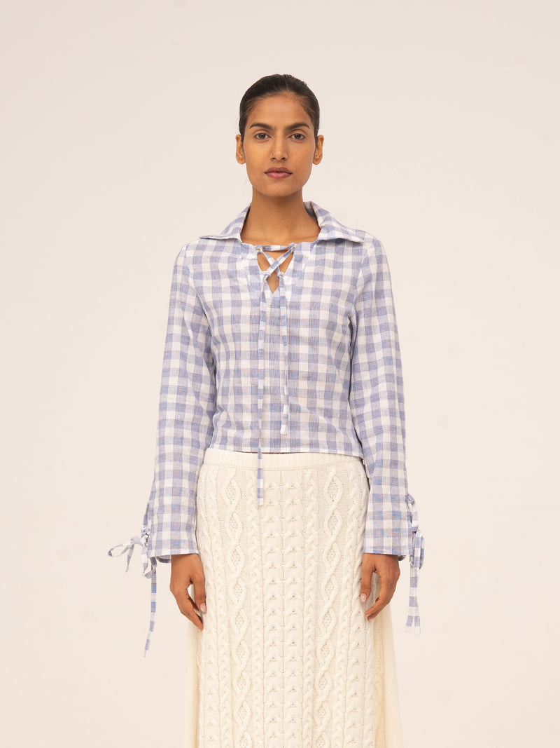 Camisa de manga larga con estampado de cuadros vichy en tonos azul claro y blanco, escote con lazada y puños ajustables.