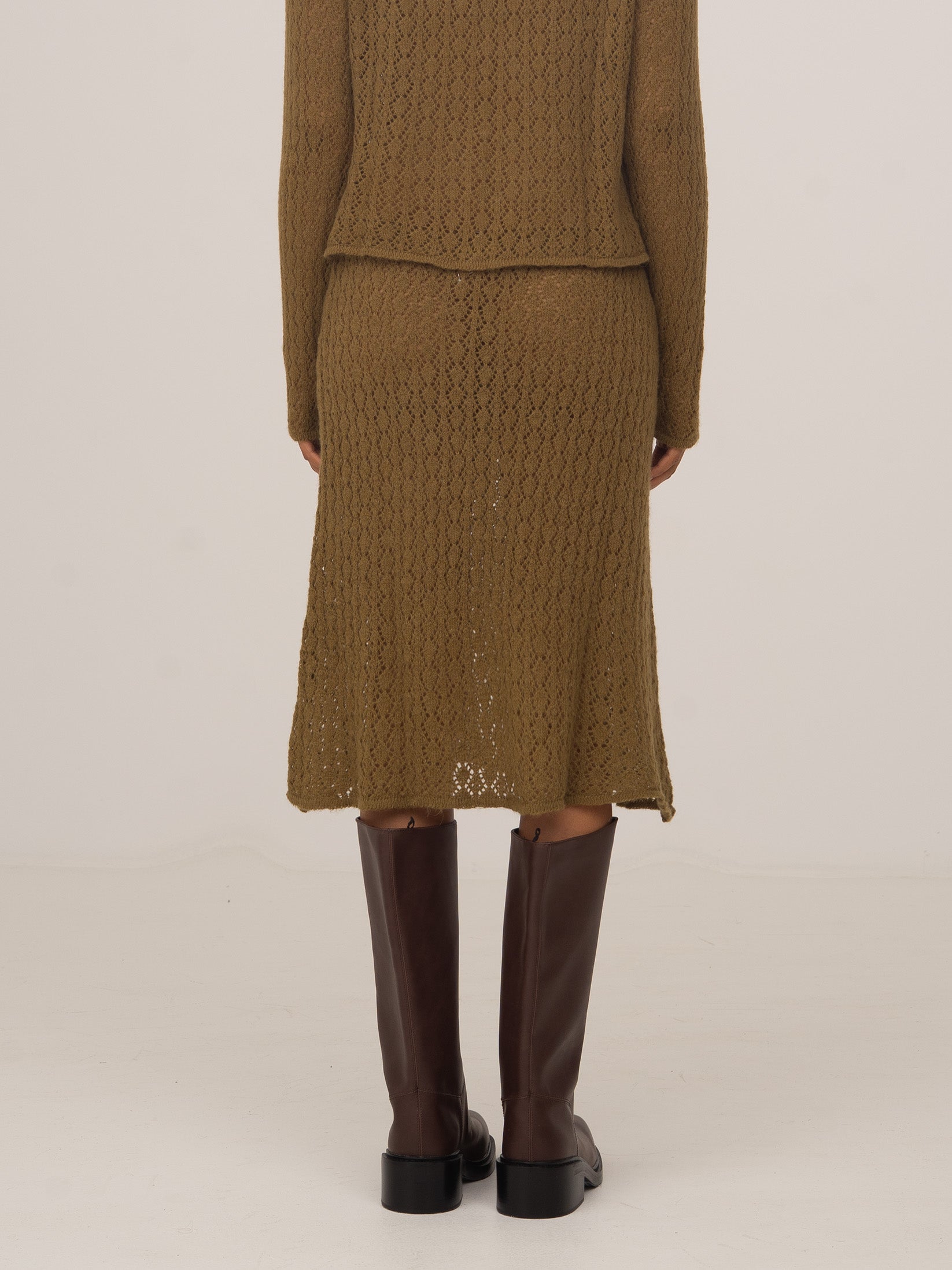 Vista trasera de falda midi de punto verde con textura trenzada, combinada con botas altas marrones