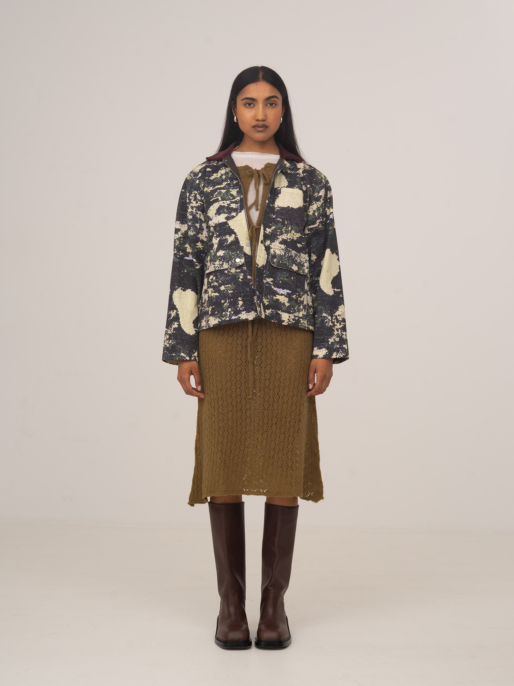 Mujer con falda midi de punto verde, combinada con chaqueta estampada en tonos oscuros y botas altas marrones