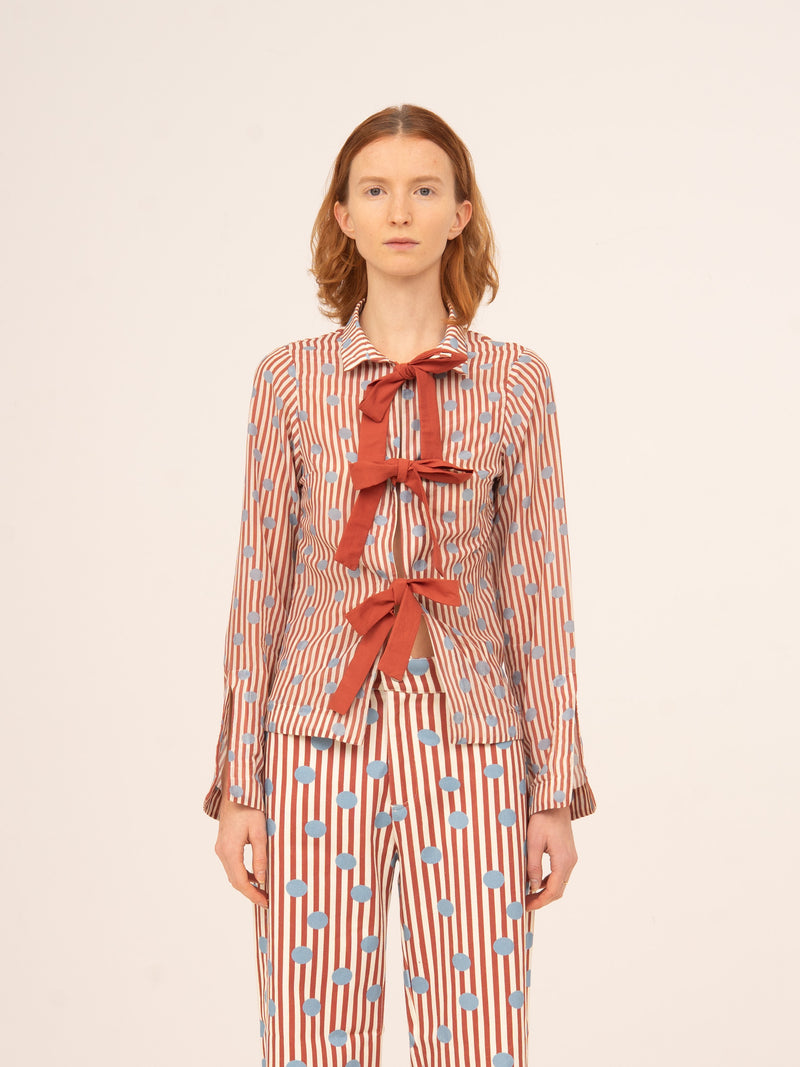 Blusa femenina de manga larga con estampado de rayas en tonos rojos y azules, detalle de lazos frontales en contraste rojo y corte entallado, elegante y original, ideal para looks sofisticados, conjuntos especiales o estilismos con un aire romántico y distintivo.
