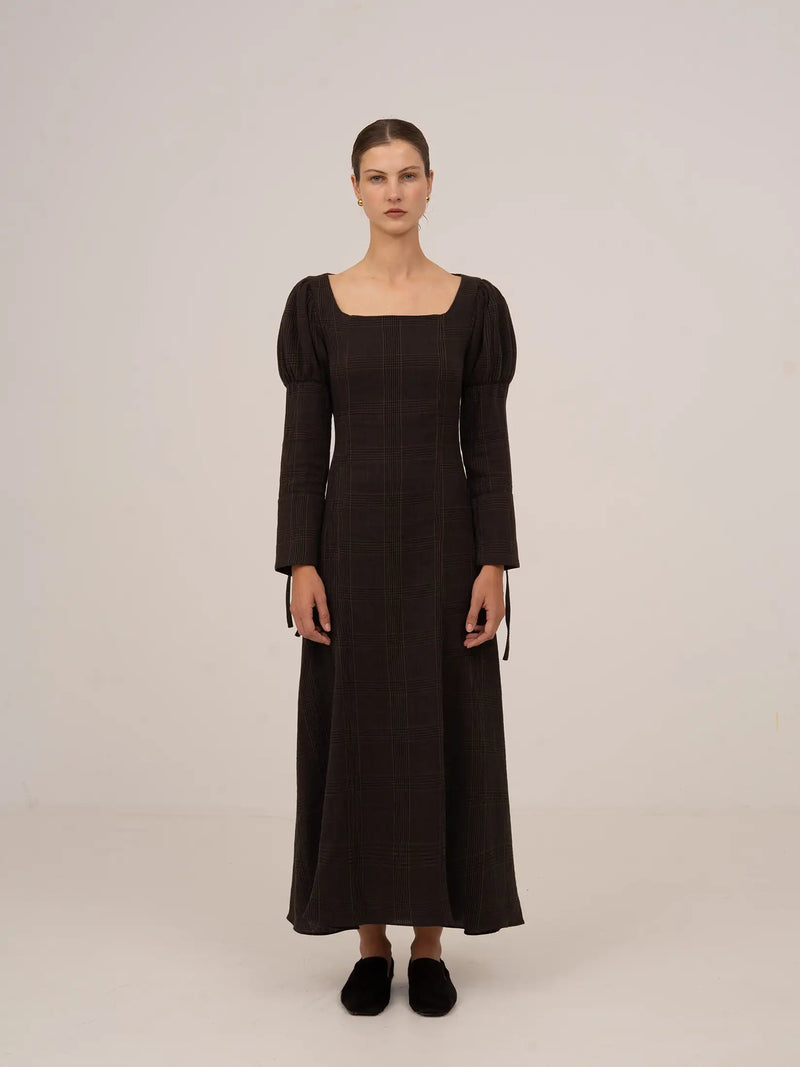 Vestido largo de cuadros en tono marrón oscuro, con escote cuadrado, mangas largas ligeramente abullonadas y silueta recta de caída elegante.