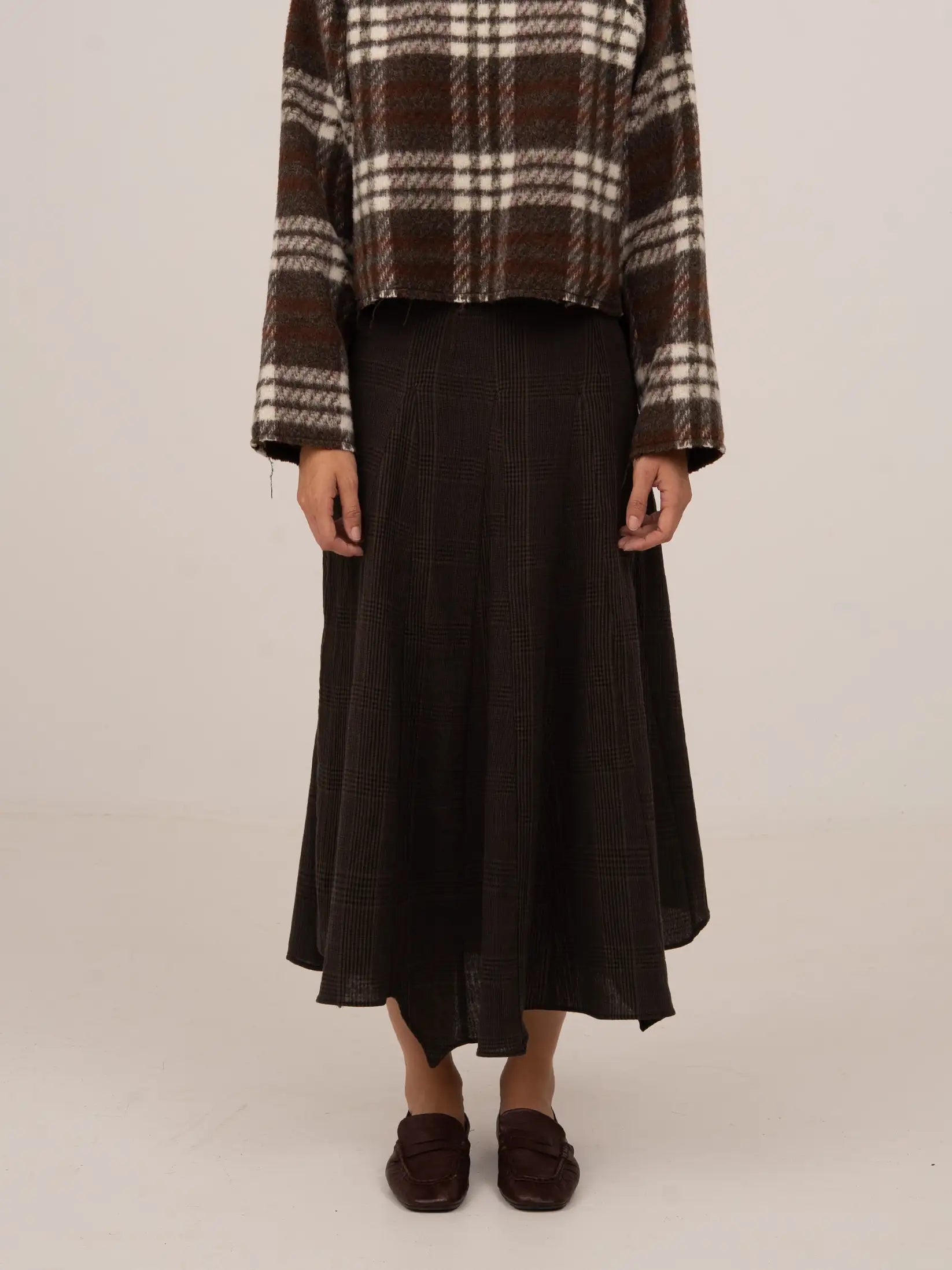 Falda midi de cuadros en tonos marrón oscuro, con caída fluida y silueta ligeramente evasé de largo medio.